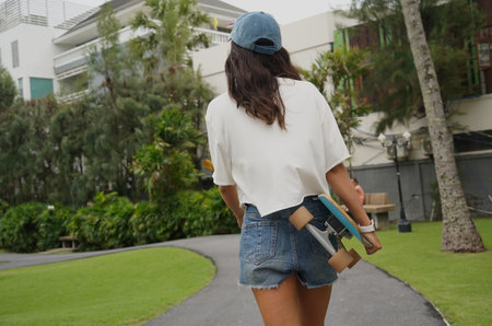 A woman is walking at the city park while carrying a skateboard in her hands