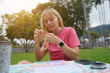 Young woman beading colorful bracelets outdoors in a park