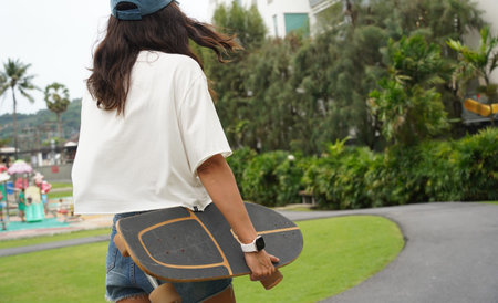 A woman is walking at the city park while carrying a skateboard in her hands