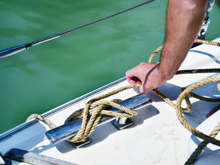 Male captain on deck of sailboat opening sails pulling the rope