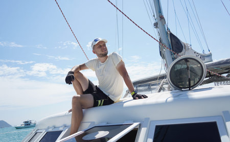 A man is calmly sitting on the deck of a beautiful sailboat