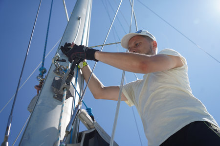Male captain on deck of sailboat opening sails pulling the ropeの写真素材
