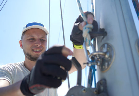Male captain on deck of sailboat opening sails pulling the rope