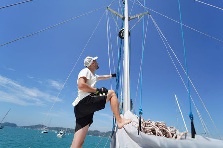 Male captain climbing mast of sailboat to check sails