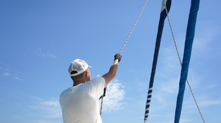 Male captain on deck of sailboat opening sails pulling the ropeの写真素材