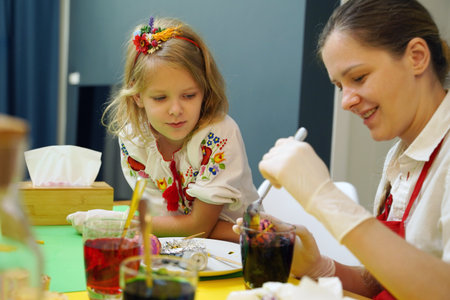 Mother and daughter at the table in traditional Ukrainian costumes painting eggs for Easterの写真素材