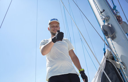 Male captain on deck of sailboat opening sails pulling the ropeの写真素材