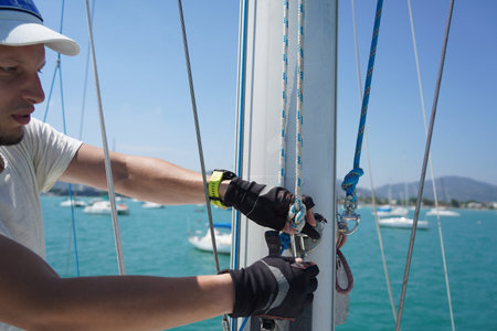 Male captain on deck of sailboat opening sails pulling the rope