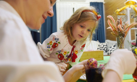 Mother and daughter at the table in traditional Ukrainian costumes painting eggs for Easter