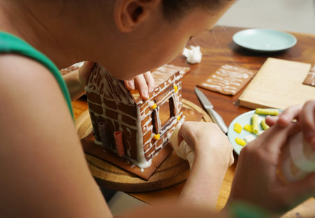 Mother and daughter at the table cooking gingerbread house for Christmasの写真素材