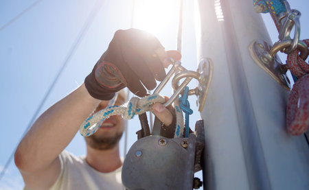 Male captain on deck of sailboat opening sails pulling the rope
