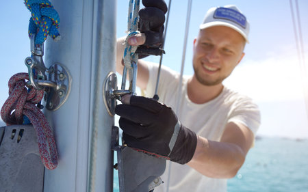 Male captain on deck of sailboat opening sails pulling the rope