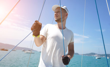 Male captain on deck of sailboat opening sails pulling the rope