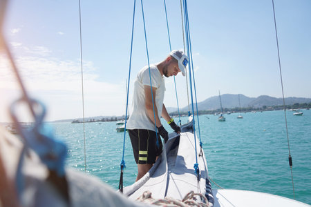 Male captain on deck of sailboat unpacking sails pulling zipper