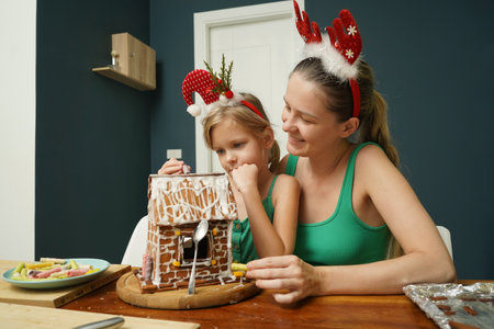 Mother and daughter at the table cooking gingerbread house for Christmasの写真素材