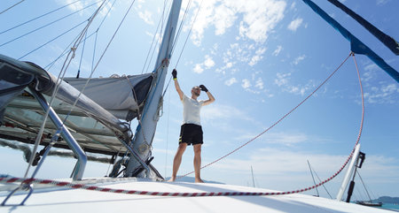 Male captain on deck of sailboat opening sails pulling the rope