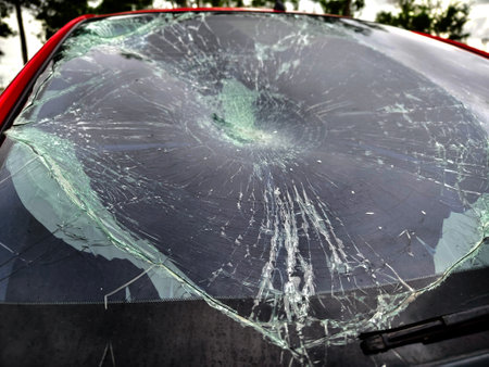 Shattered and broken windshield on a bright red car showcasing the damage to its glass surfaceの写真素材