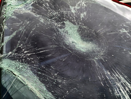 Shattered and broken windshield on a bright red car showcasing the damage to its glass surfaceの写真素材