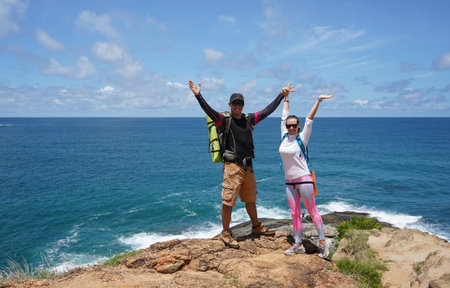 A young couple are hiking on a rugged rocky cliff that offers a view of the oceanの写真素材