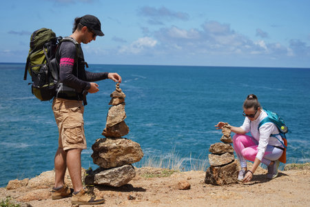 A man and a woman are carefully stacking rocks in an artistic manner near the ocean.