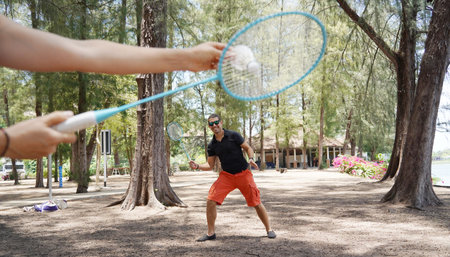 A man and a young woman are playing badminton together in a park