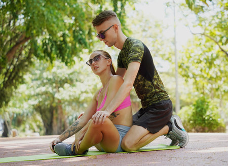 A man is providing assistance to a woman as she stretches her legs on a colorful yoga matの写真素材