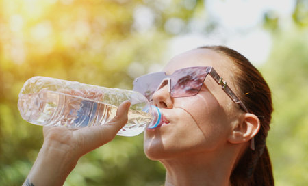 A man and a woman drinking refreshing water from bottles after jogging together in a park