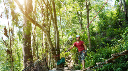 A man is walking across a challenging ropes course in the extreme park