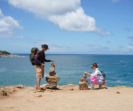 A man and a woman are carefully stacking rocks in an artistic manner near the ocean.の写真素材