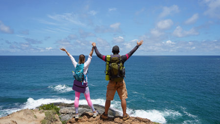 A young couple are hiking on a rugged rocky cliff that offers a view of the oceanの写真素材