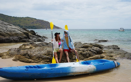 A young couple at the sandy beach holding kayak paddles and ready for a fun trip on the water