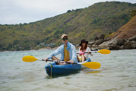 The young couple are happily navigating together in a light blue kayak with yellow paddlesの写真素材