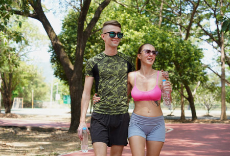 A man and a woman drinking refreshing water from bottles after jogging together in a parkの写真素材