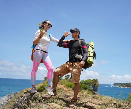 A young couple are hiking on a rugged rocky cliff that offers a view of the oceanの写真素材