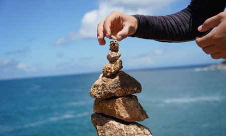 A man and a woman are carefully stacking rocks in an artistic manner near the ocean.の写真素材