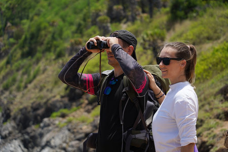 A man and a woman are intently looking through binoculars at something interesting in the distance
