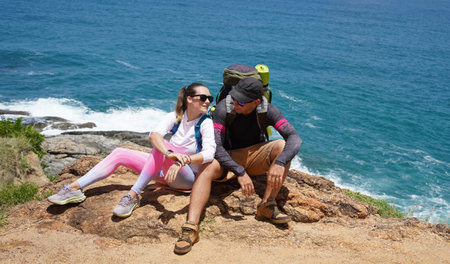 A young couple are hiking on a rugged rocky cliff that offers a view of the oceanの写真素材