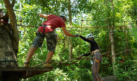 A man and a woman is walking across a challenging ropes course in the extreme parkの写真素材