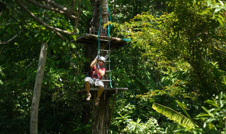 A man is enjoying an exhilarating ride on a zip line that traverses the thick woods surrounding himの写真素材