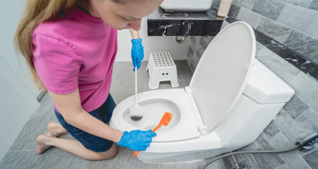Young housewife diligently scrubs and cleans the toilet bowl in bathroom
