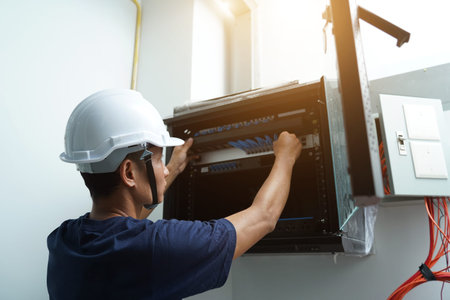 A maintenance technician works in a server room with a fiber optic hub