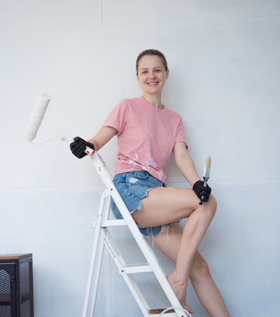Young woman painting indoors wall with roller using stepladderの写真素材