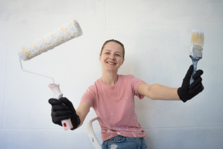Young woman painting indoors wall with roller using stepladderの写真素材