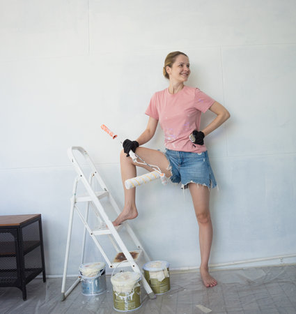 Young woman painting indoors wall with roller using stepladderの写真素材