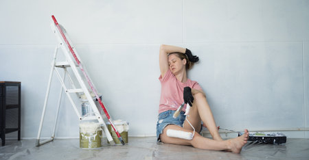Young woman painting indoors wall with roller using stepladderの写真素材