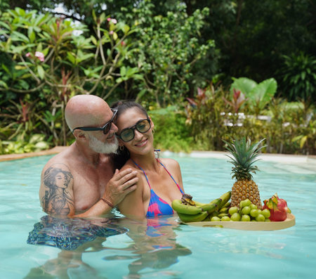 A man and woman with tray of a fresh fruits in a swimming poolの写真素材