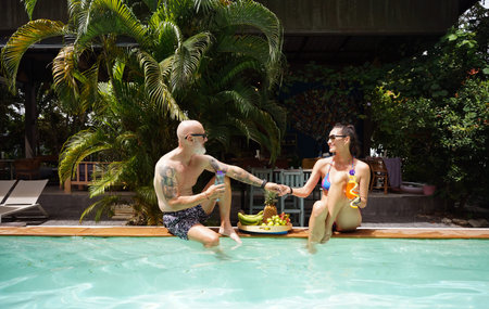 A man and a woman sit by the pool with cocktails and fruit.の写真素材