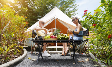 A man and woman are joyfully drinking beer and playing guitar near a cozy tent at glamping.