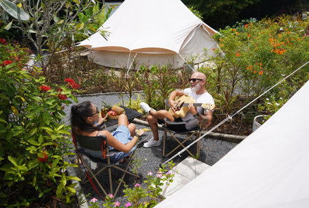 A man plays guitar for a woman near a cozy tent at a glamping site.の写真素材