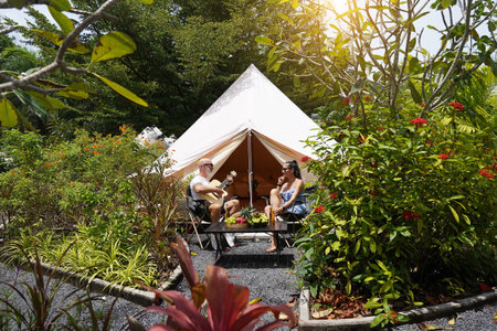 A man plays guitar for a woman near a cozy tent at a glamping site.の写真素材
